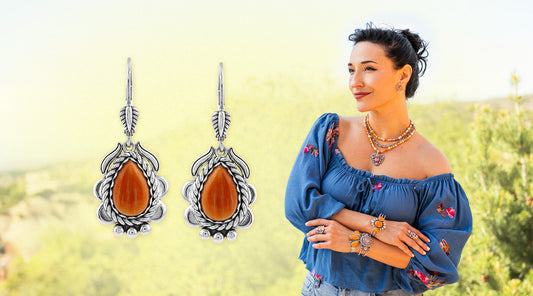 American West Jewelry sterling silver orange spiny oyster teardrop earrings alongside a woman wearing orange spiny oyster layered necklace with heart pendant, rings, and bracelets styled in an embroidered blue off-shoulder blouse